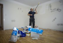 Að vinna svart Málari stendur á parketi og mundar málningarrúllu