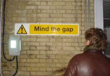 Maður stendur og horfir á skilti sem stendur á mind the gap
