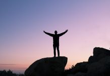 Maður stendur á kletti og baðar út höndum