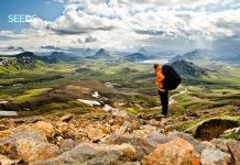 Útivistargarpur með stóran bakpoka stendur og horfir yfir fallegt landsvæði
