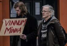 tveir menn standa saman og annar þeirra heldur á skilti með textanum „“